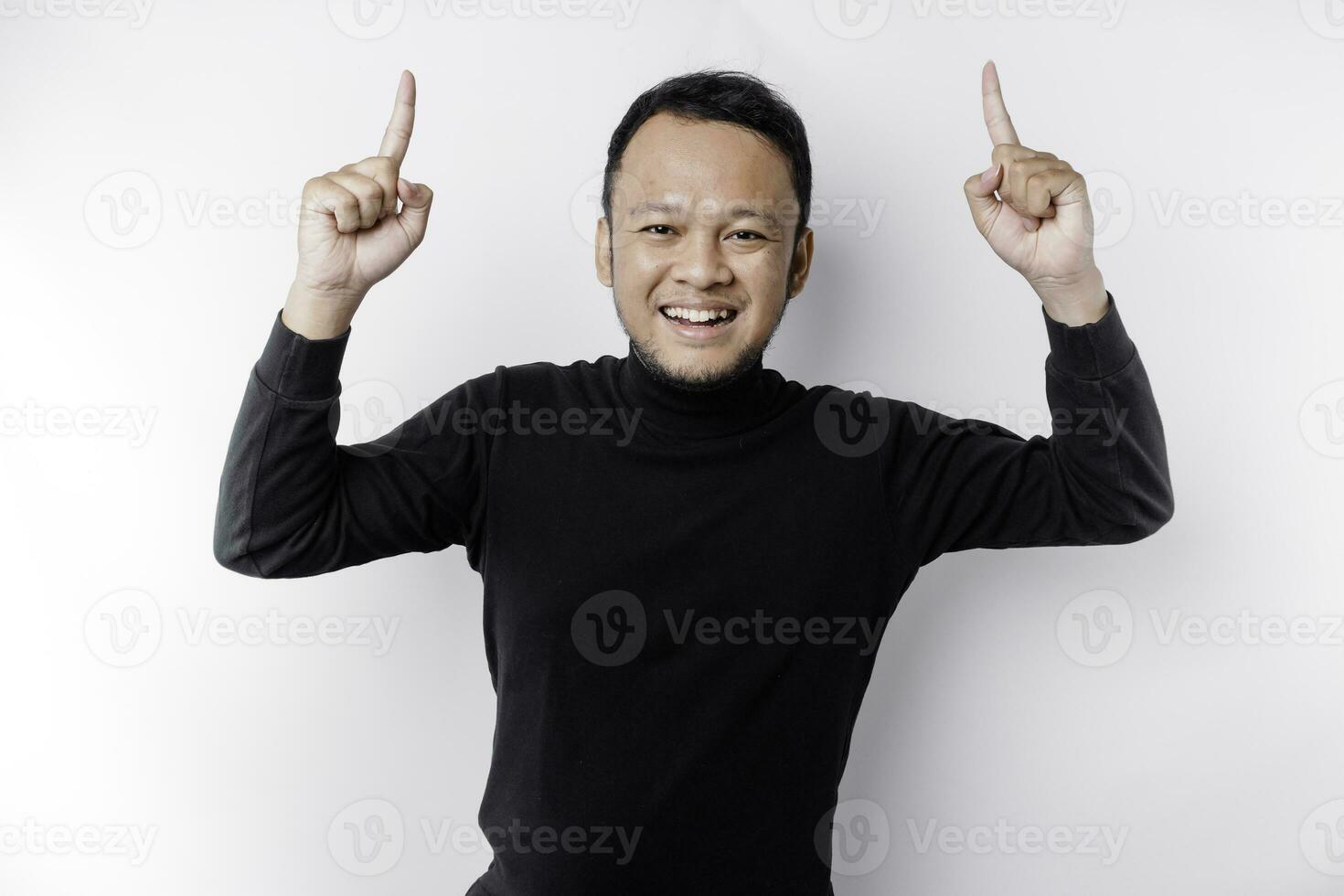 eccitato asiatico uomo indossare nero camicia puntamento a il copia spazio su superiore di lui, isolato di bianca sfondo foto