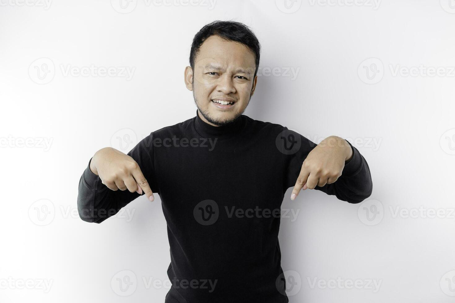 eccitato asiatico uomo indossare nero camicia puntamento a il copia spazio sotto lui, isolato di bianca sfondo foto