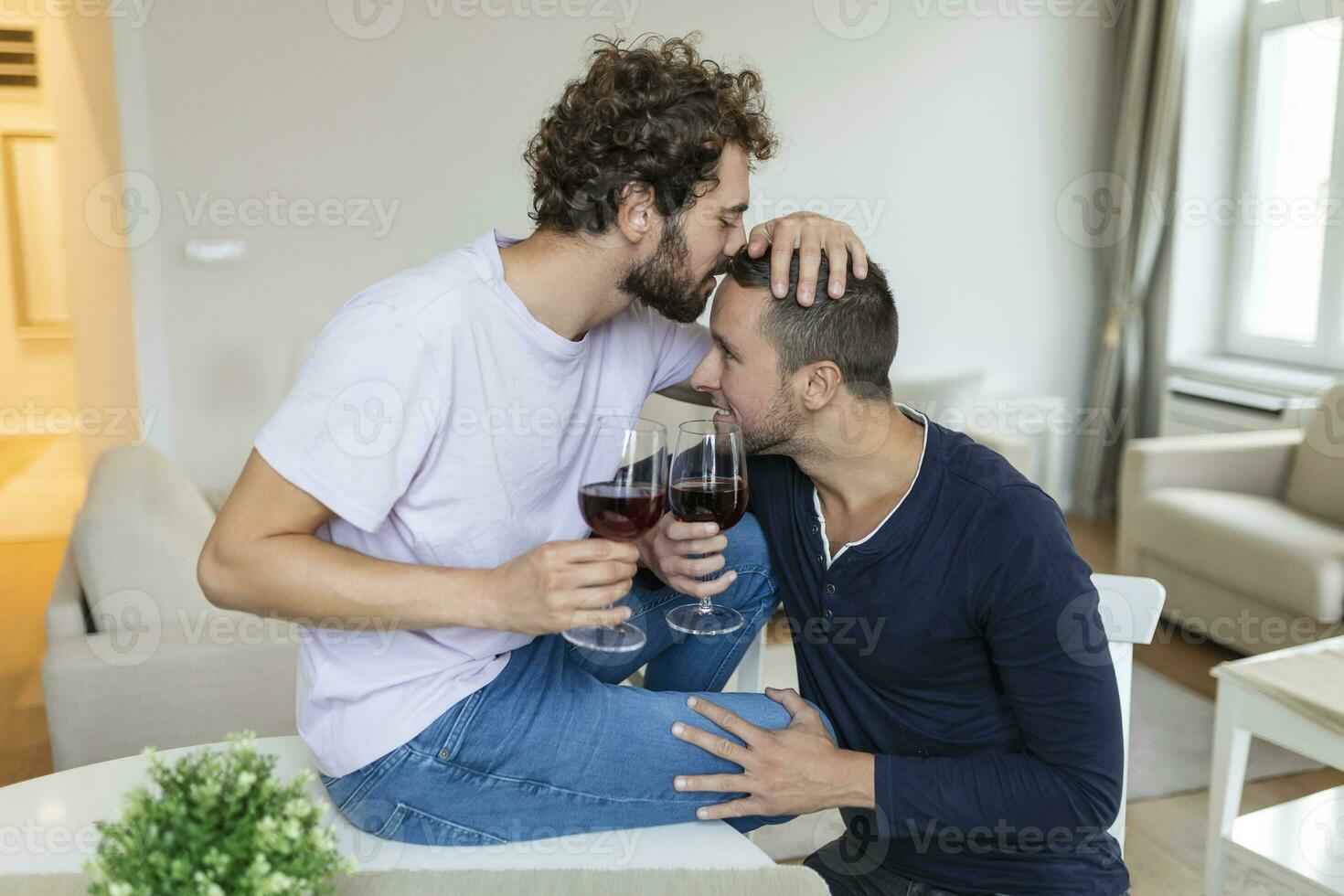 LGBTQ coppia Abbracciare una persona ogni altro e potabile vino al chiuso. Due romantico giovane maschio Gli amanti guardare a ogni altro mentre seduta insieme nel loro vivente camera. giovane gay coppia essere romantico a casa. foto