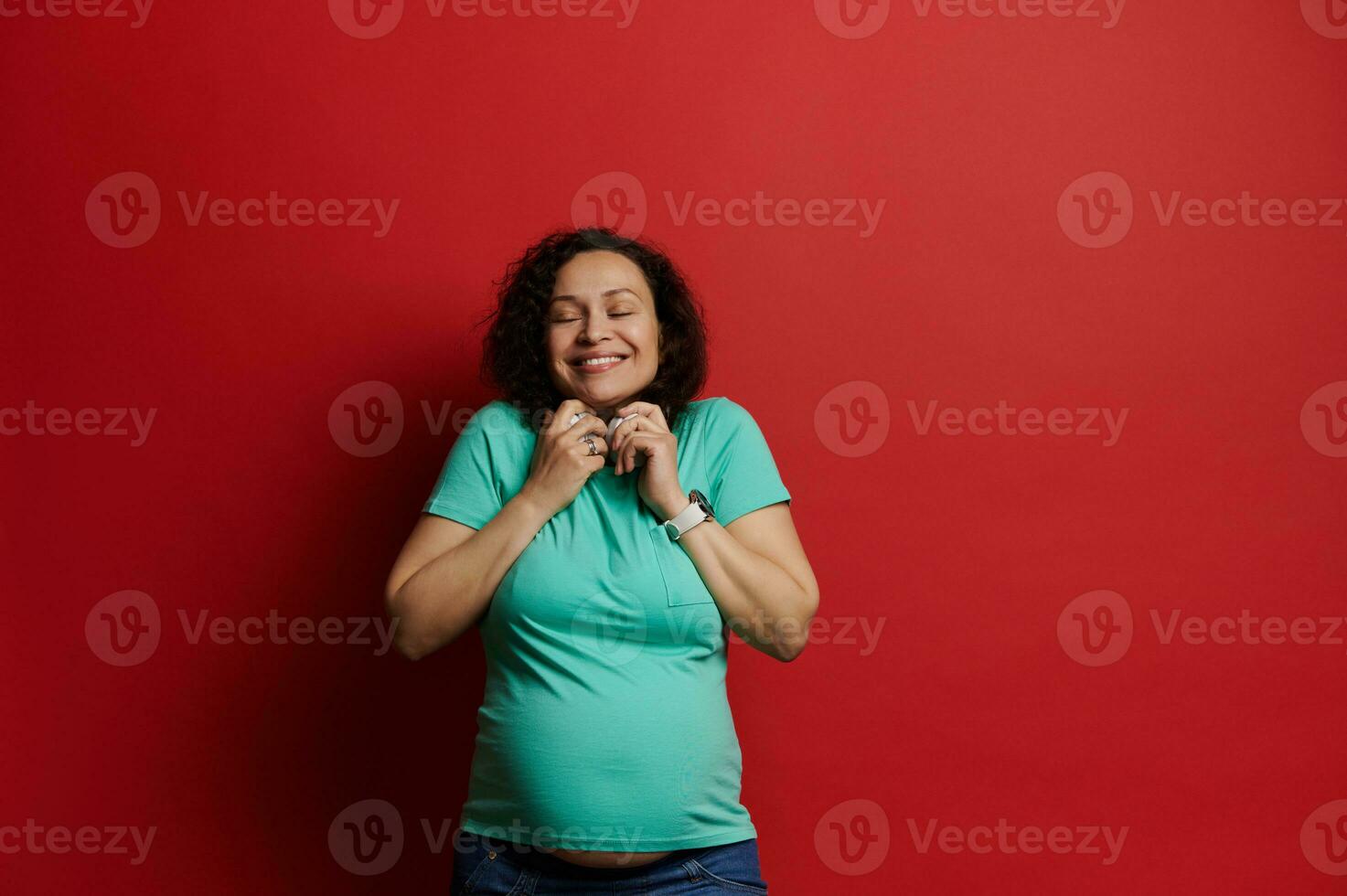 affascinante etnico incinta donna con senza fili cuffia, godendo ascoltando per un' nuovo freddo colonna sonora al di sopra di rosso sfondo foto