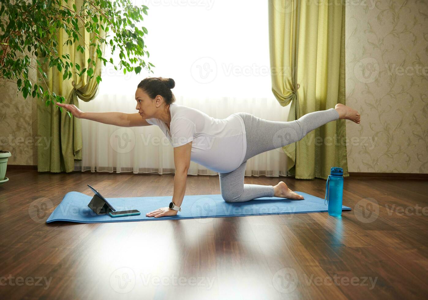 giovane incinta donna praticante in linea gravidanza yoga, fare prenatale uccello solare, bird-dog posa nel il vivente camera interno foto