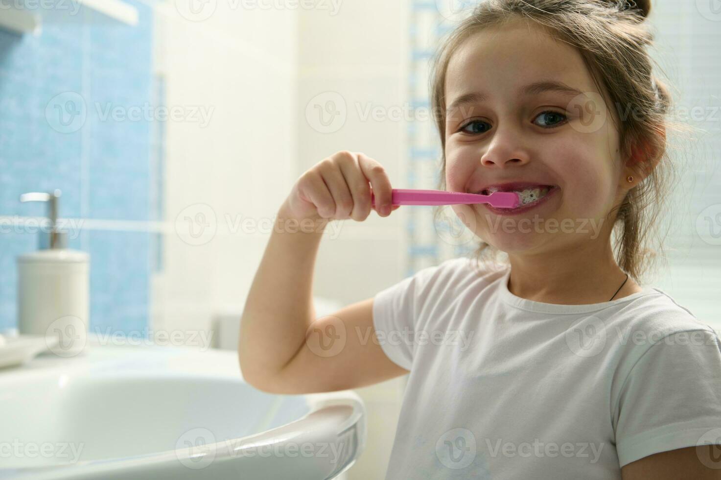 avvicinamento bello bambino ragazza spazzolatura denti, sorridente con bellissimo Sorridi guardare a telecamera. dentale Salute. orale igiene foto