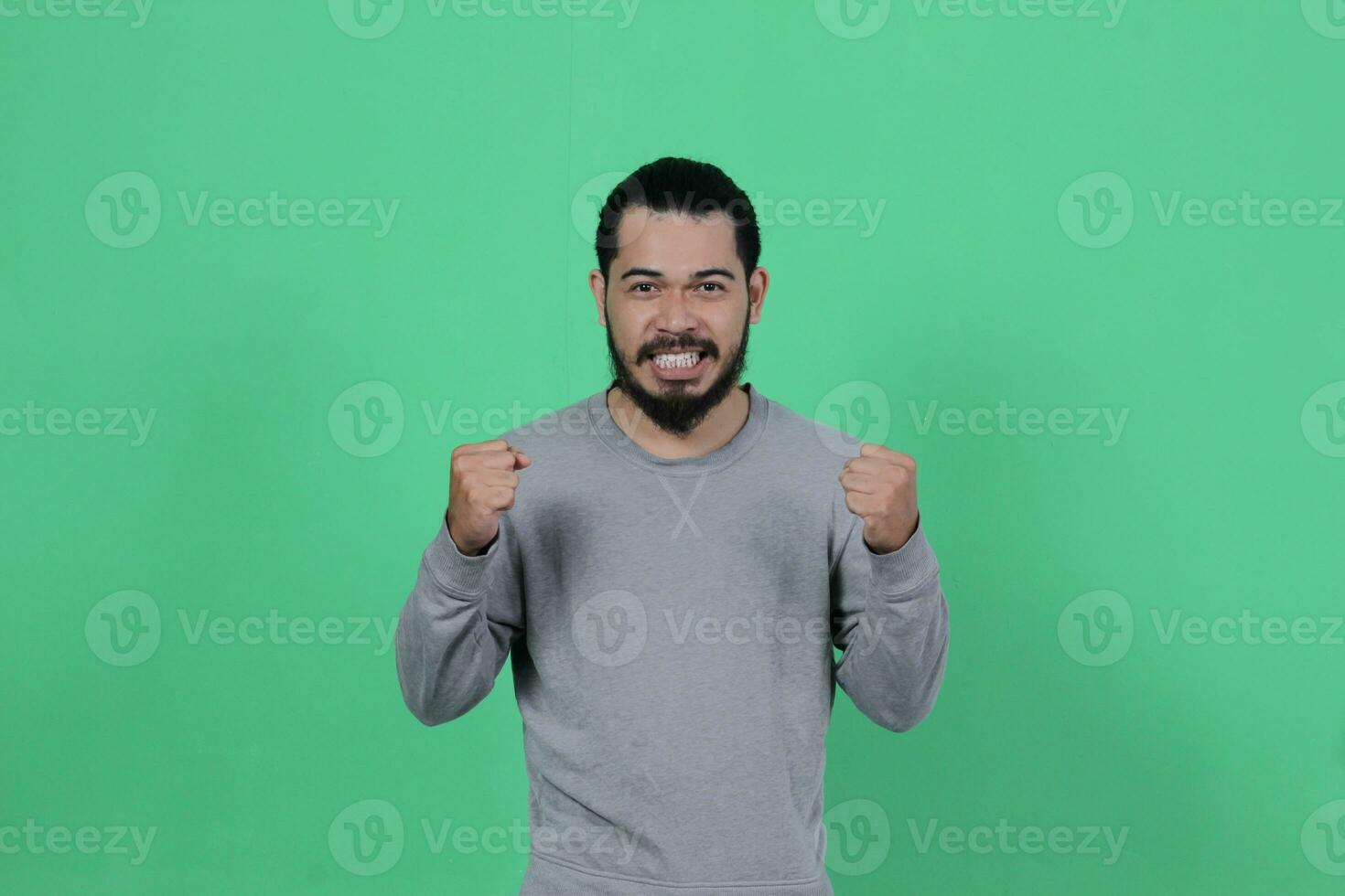 barbuto asiatico uomo pose indossare un' grigio camicia contro un' verde sfondo foto