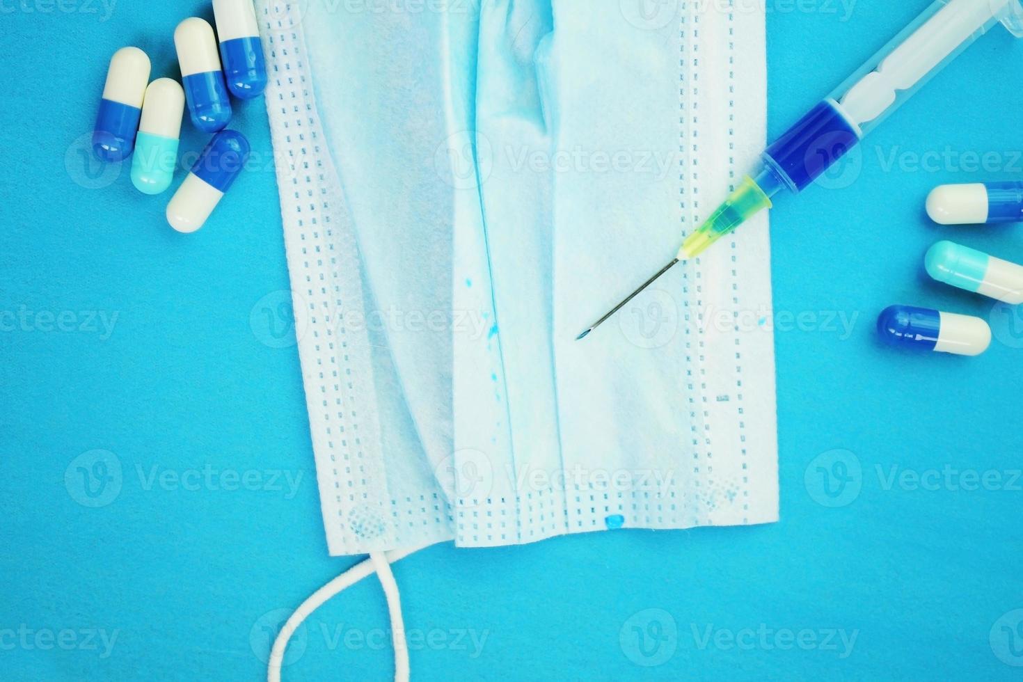 una macro dettagliata di una siringa da pillole con ago su una maschera medica con sfondo blu foto
