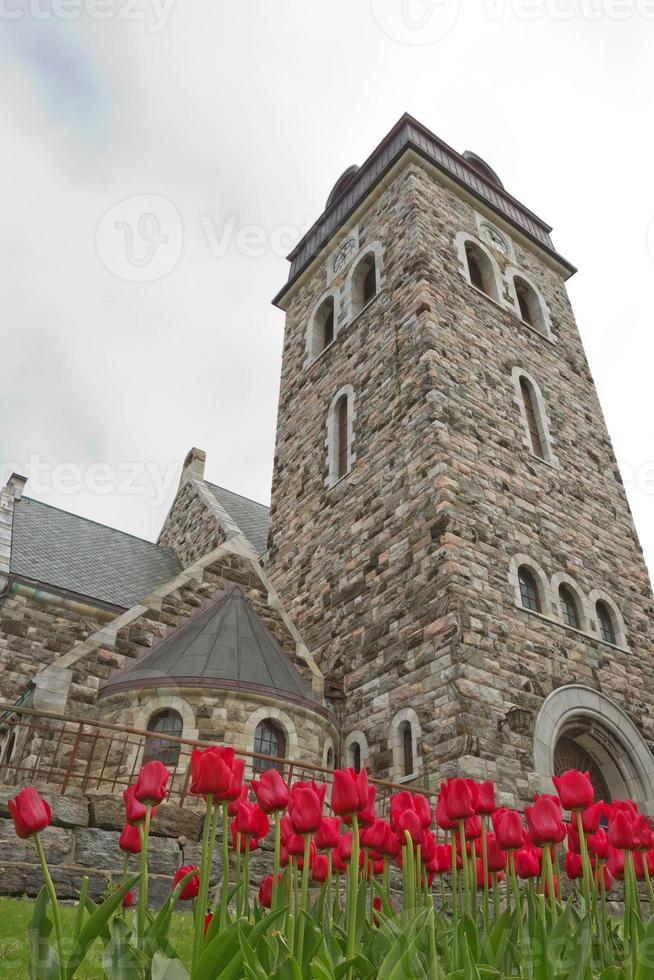 vista di una storica chiesa in pietra in alesund norvegia con tulipani rossi in primo piano foto