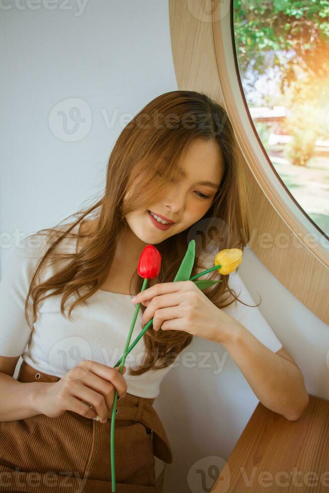 ritratto di bella signora Tenere tulipani nel mani. giovane romantico donna vicino occhi sorridente e annusando bellissimo di fiori, seduta soddisfatto nel bar. concetto di femmina bellezza, primavera e femminilità. foto