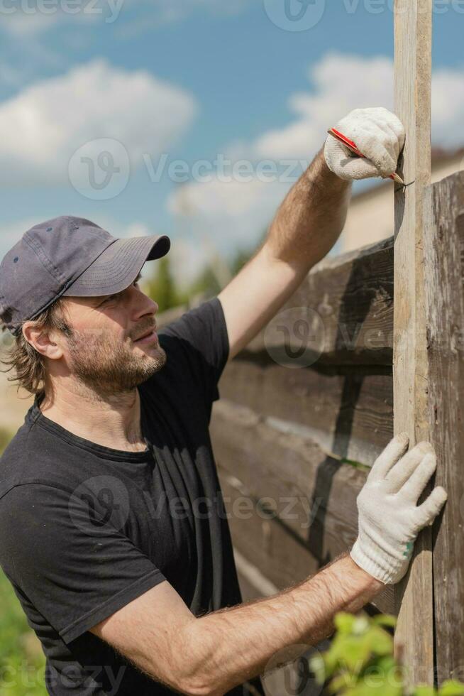 uomo costruisce sezioni di recinto in giro il suo cortile su di tavole - estate casa faccende nel il Giardino dietro la casa foto