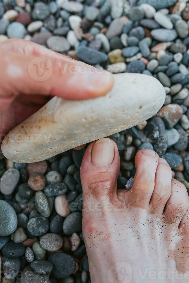 uomo macinazione il suo miniatura con un' pietra - rotte, trasandato chiodo - peeling e pedicure su il spiaggia foto