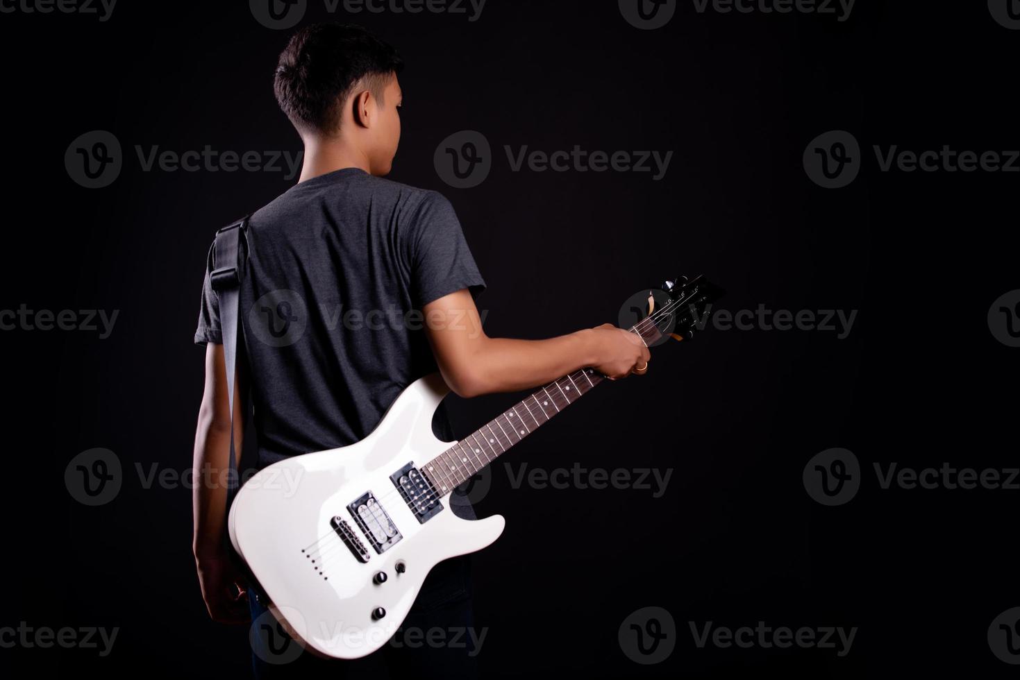 giovane uomo in giacca di pelle nera con chitarra elettrica su sfondo nero in studio foto