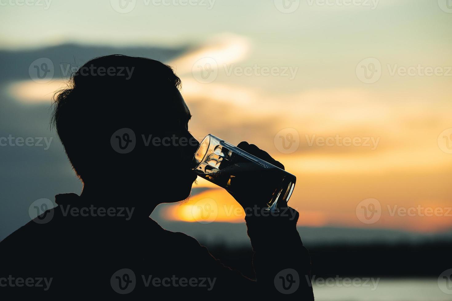 silhouette uomo che tiene la birra in vetro con sfondo tramonto foto