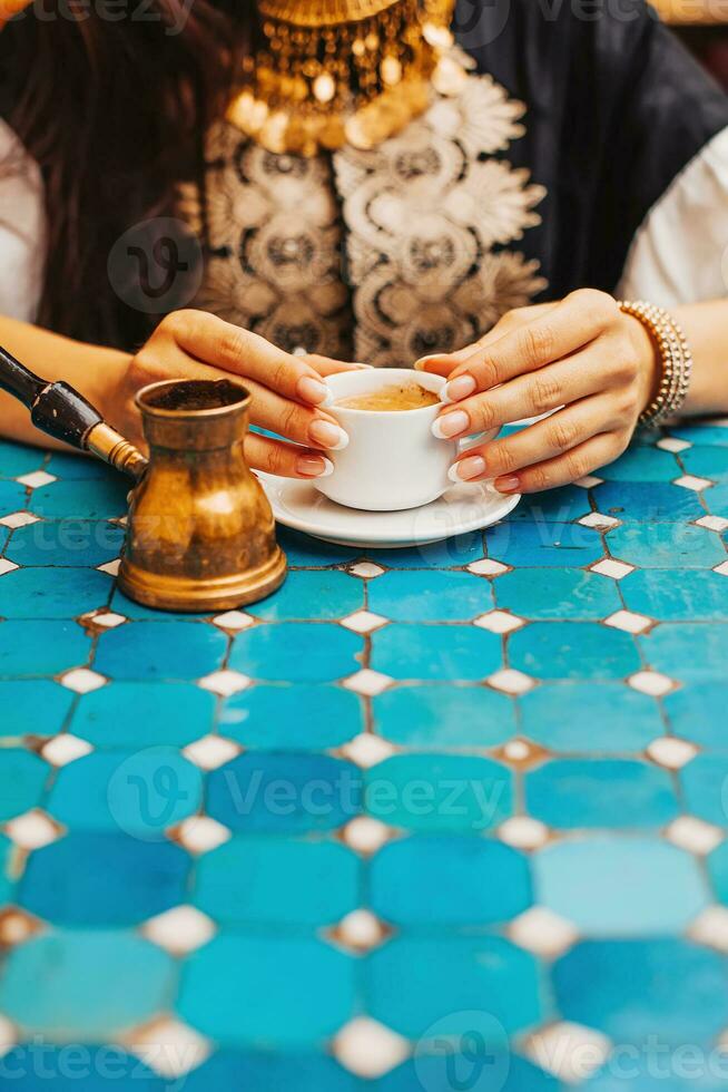 avvicinamento foto di donna Tenere un' tazza di Turco caffè nel un' bar con turchese piastrelle tavolo