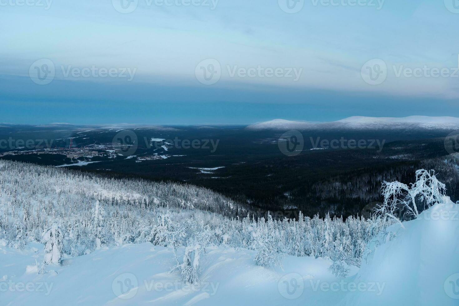 un' innevato pendenza di il polare collina nel il inverno presto nel il mattina con un' lontano Visualizza di Kandalaksha, un' porta città nel settentrionale Russia. inverno polaris paesaggio. freddo inverno tempo atmosferico. foto