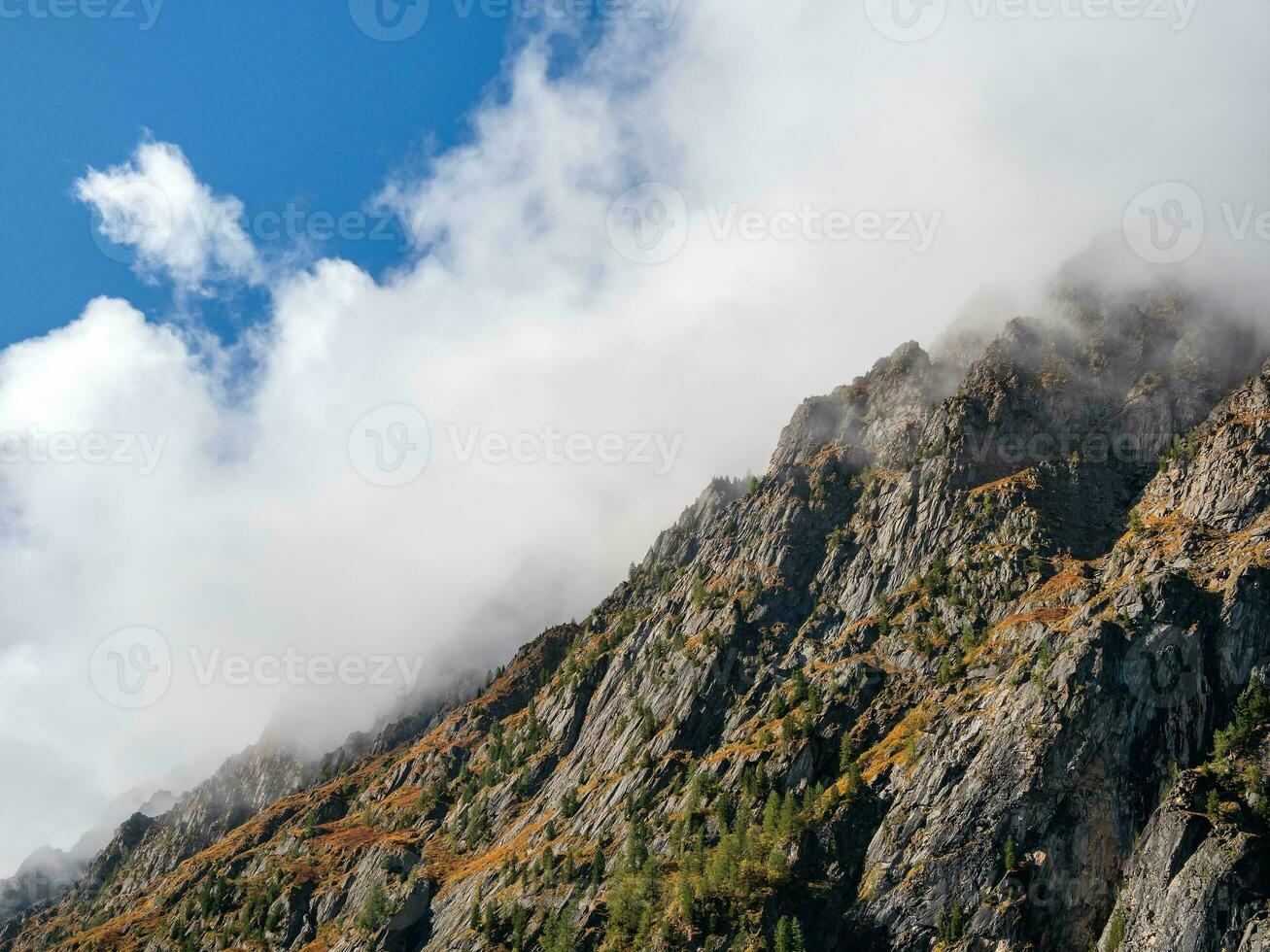 cresta di il montagna sotto bianca Basso nuvole. spettrale atmosferico Visualizza per grande scogliera nel nuvoloso cielo. Basso nuvole tra gigante roccioso montagne.naturali sfondo con alto montagne, un' ripido montagna pendenza foto