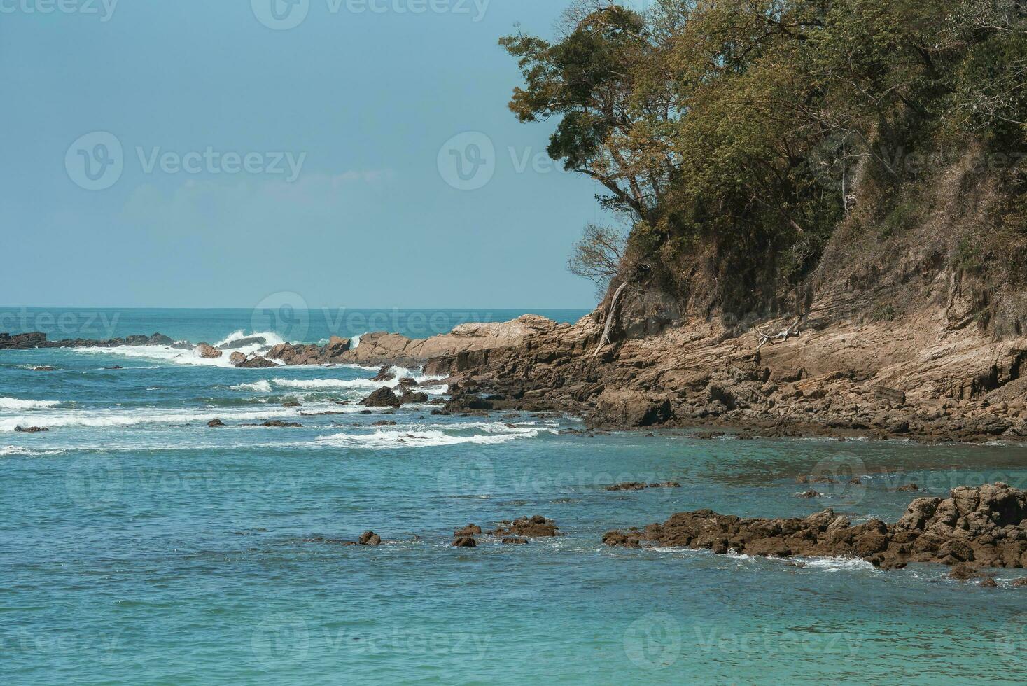 bellissimo Visualizza di onde spruzzi su roccioso spiaggia sotto chiaro blu cielo foto
