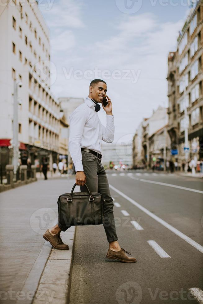 giovane uomo d'affari afroamericano utilizzando un telefono cellulare mentre si attraversa una strada foto