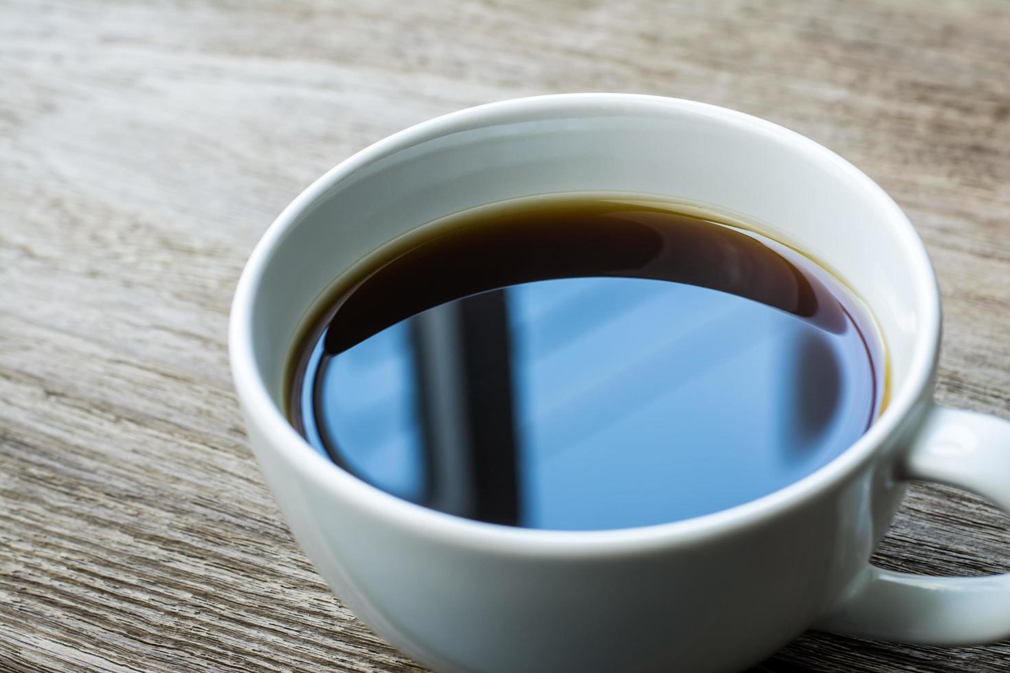 primo piano della tazza di caffè sulla tavola di legno e la finestra riflessa sul caffè nero foto