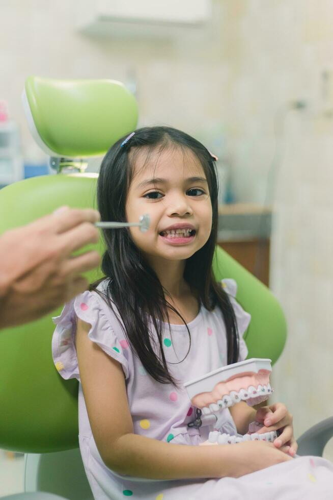 asiatico dentista e asiatico ragazzo conoscenza di bretelle uso dentiera modello quando madre sedersi di nel dentale clinica foto