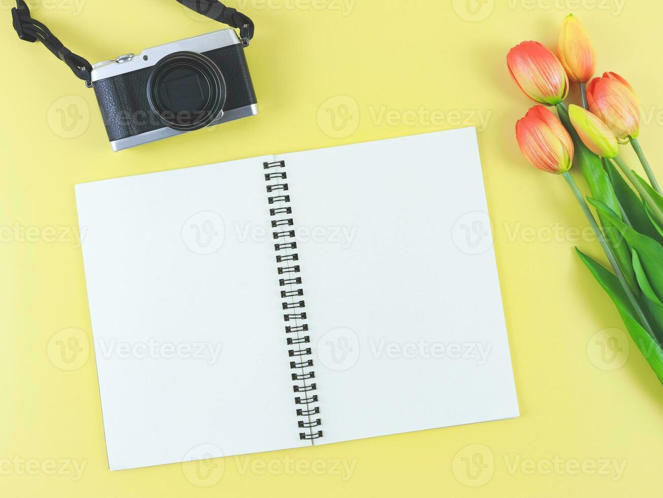 piatto posare di vuoto pagina ha aperto taccuino, digitale telecamera e rosso giallo tulipani fiori su giallo sfondo con copia spazio. foto