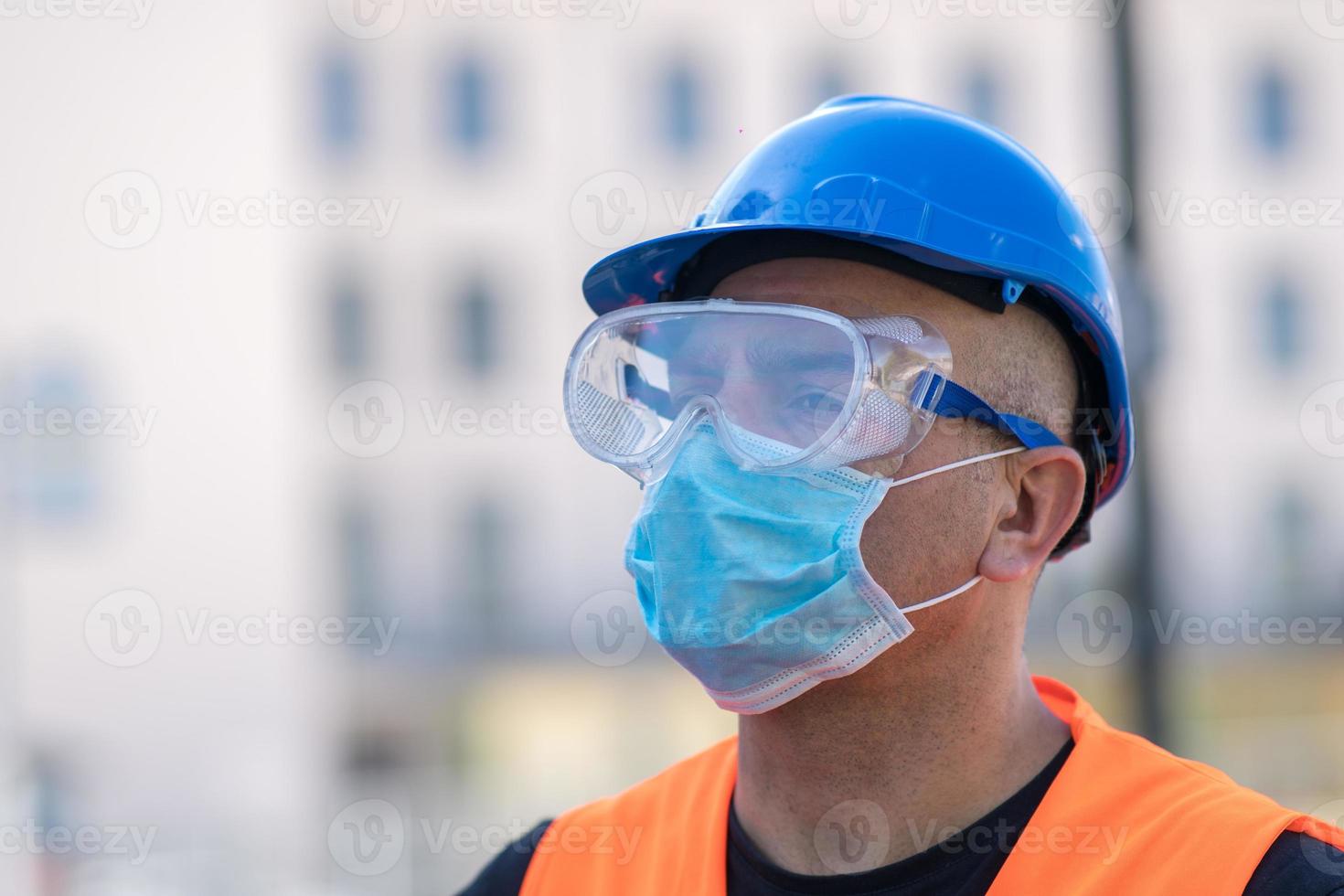 operaio edile che indossa elmetto blu, giubbotto riflettente e maschera chirurgica protettiva foto