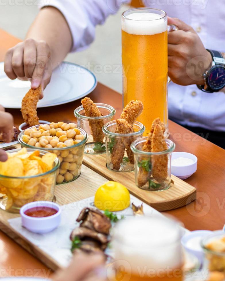 uomo che immerge il pollo fritto nel ketchup mentre si tiene un boccale di birra foto