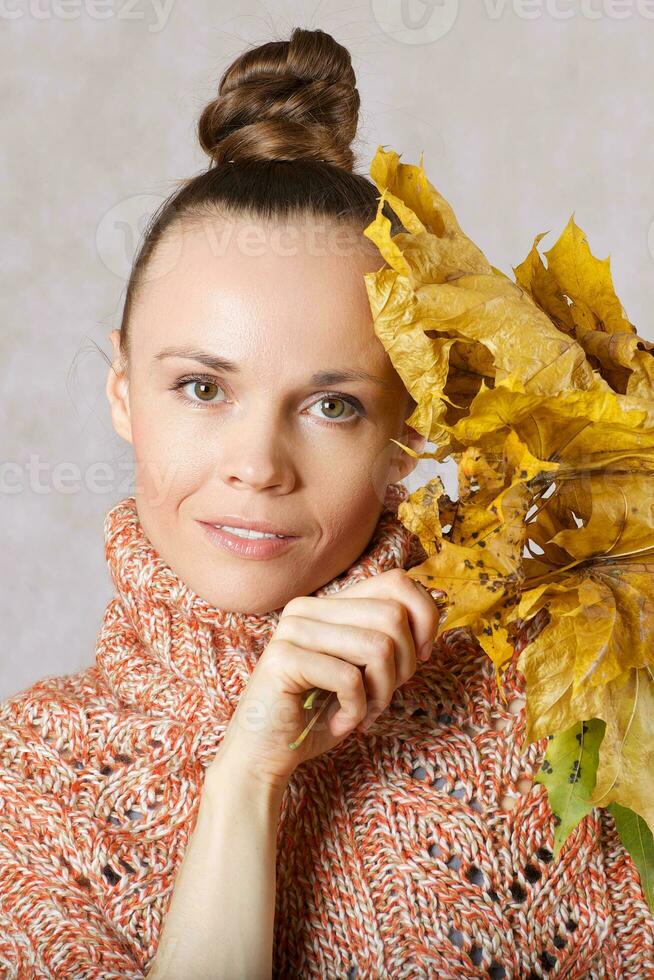 giovane caucasico signora fra 30 e 40 anni vestito nel un' a maglia poncho con disidratato acero le foglie. foto