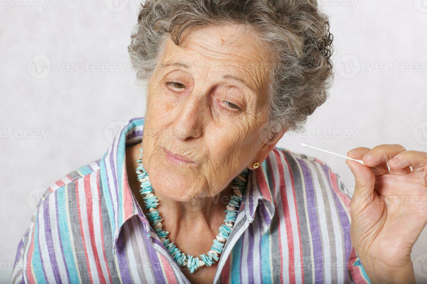 vecchio donna è pulizia sua orecchie con cotone tampone foto