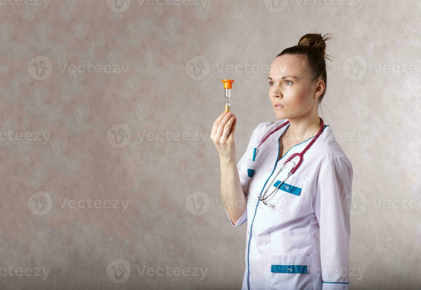 giovane femmina medico vestito nel un' bianca medico uniforme mantiene un' sabbia orologio foto