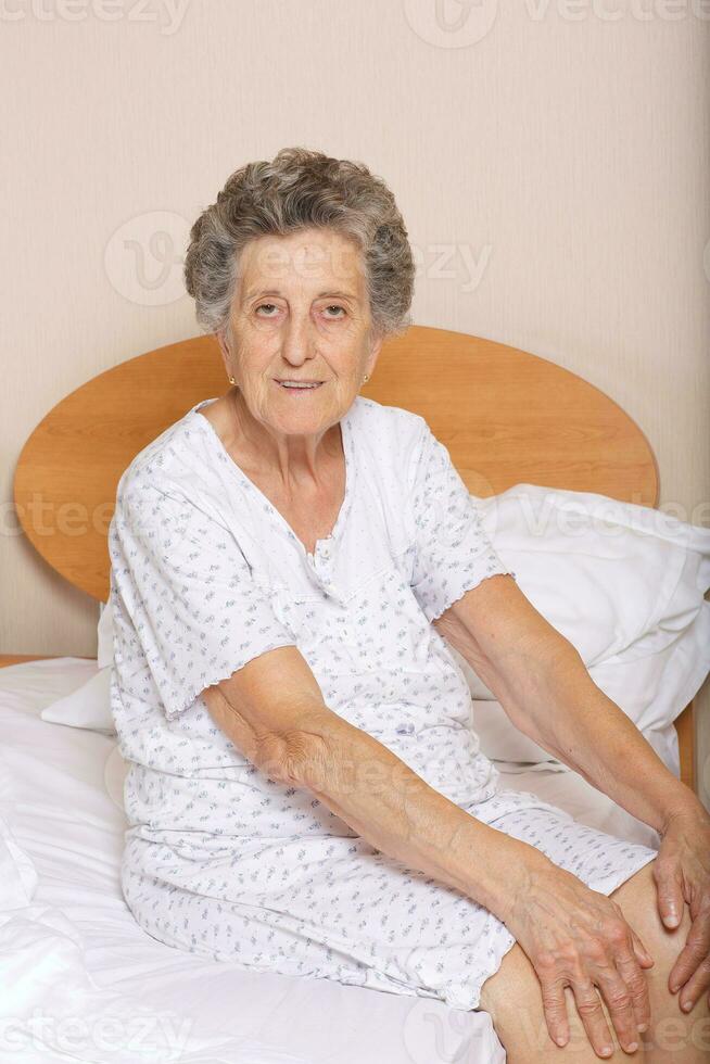 anziano donna è seduta nel sua letto foto