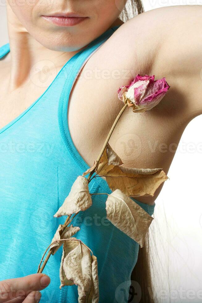 un' giovane donna fra mantiene disidratato rosa vicino per sua ascella. foto