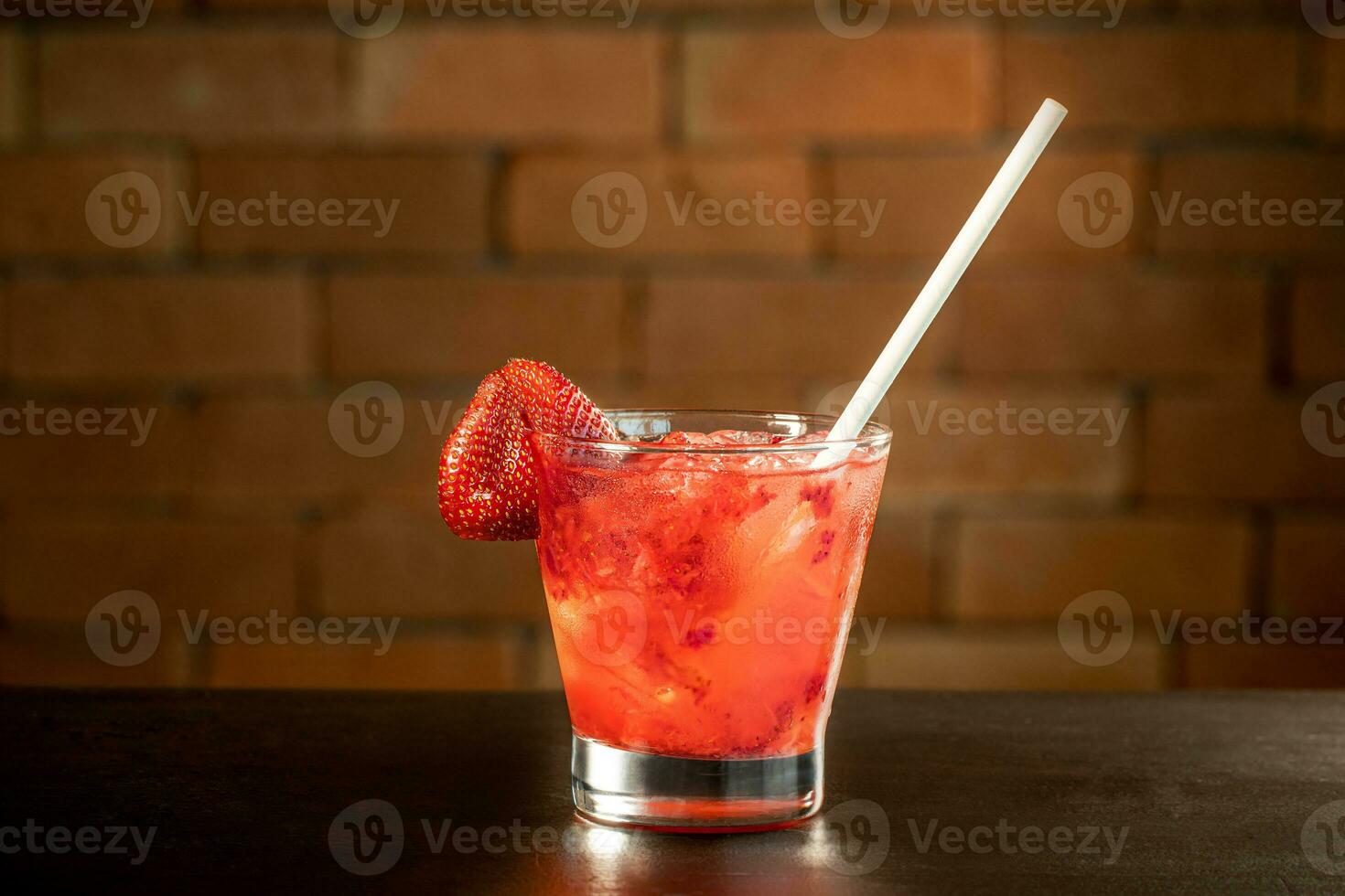 bicchiere di fragola Caipirinha bevanda su un' tavolo nel davanti di un' mattone parete con spazio per testo foto