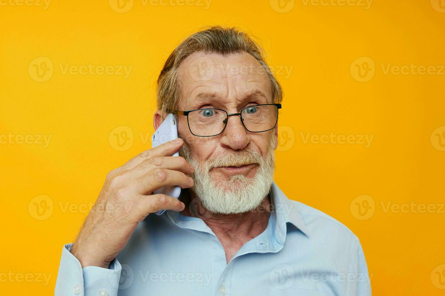 anziano dai capelli grigi uomo nel un' blu camicia e bicchieri parlando su il Telefono isolato sfondo foto