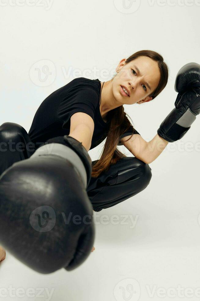 foto bella ragazza nel nero pantaloni su il pavimento boxe guanti leggero sfondo