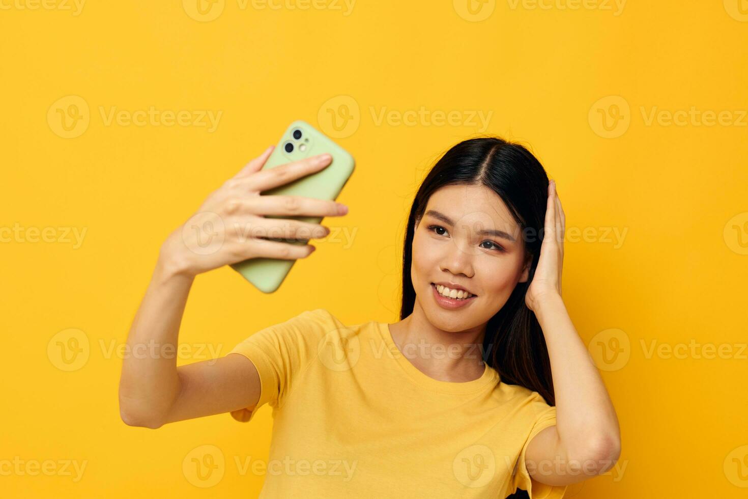 affascinante giovane asiatico donna nel un' giallo maglietta guardare a il Telefono in posa isolato sfondo inalterato foto