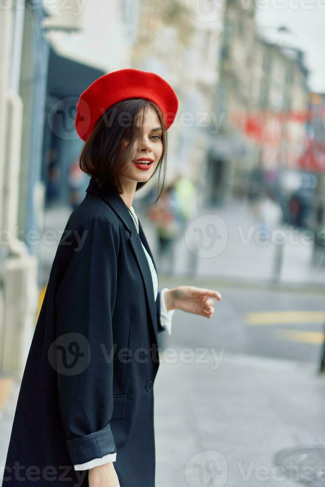 moda donna Sorridi primavera a piedi nel il città nel elegante Abiti con rosso labbra e rosso berretto, viaggiare, cinematico colore, retrò Vintage ▾ stile, urbano moda stile di vita. foto