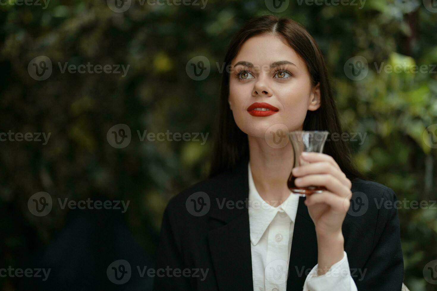 donna con rosso labbra Sorridi con denti potabile tè nel un' bar a partire dal un' Turco bicchiere boccale su il strada, estate viaggiare, vacanza nel il città foto