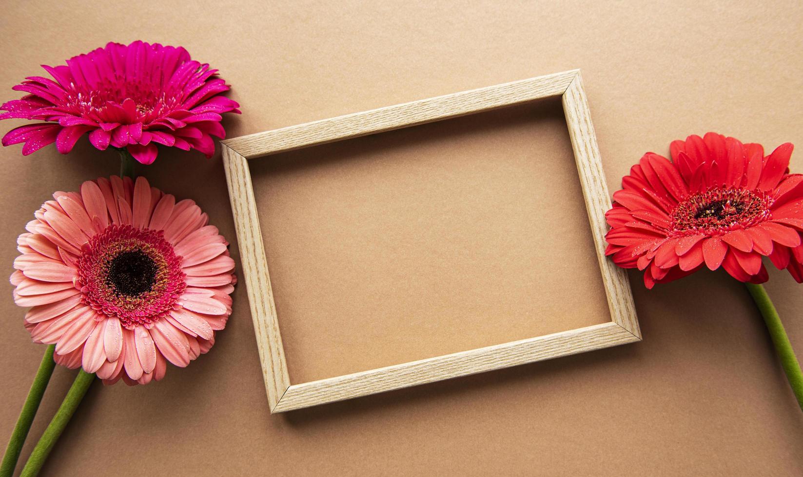 telaio in legno circondato da bellissimi fiori di gerbera su uno sfondo marrone chiaro, vista dall'alto, spazio di copia, piatto laici. foto