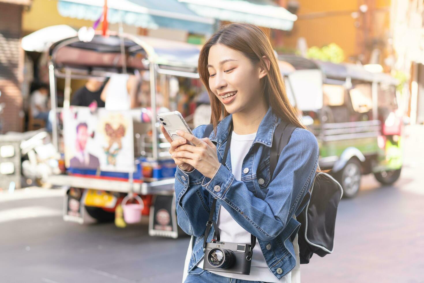 viaggiatore viaggio su vacanza fine settimana, vacanza nel estate, Sorridi attraente asiatico giovane in viaggio donna, ragazza zaino in spalla utilizzando smartphone, a piedi nel khao san strada, strada all'aperto mercato città nel bangkok. foto
