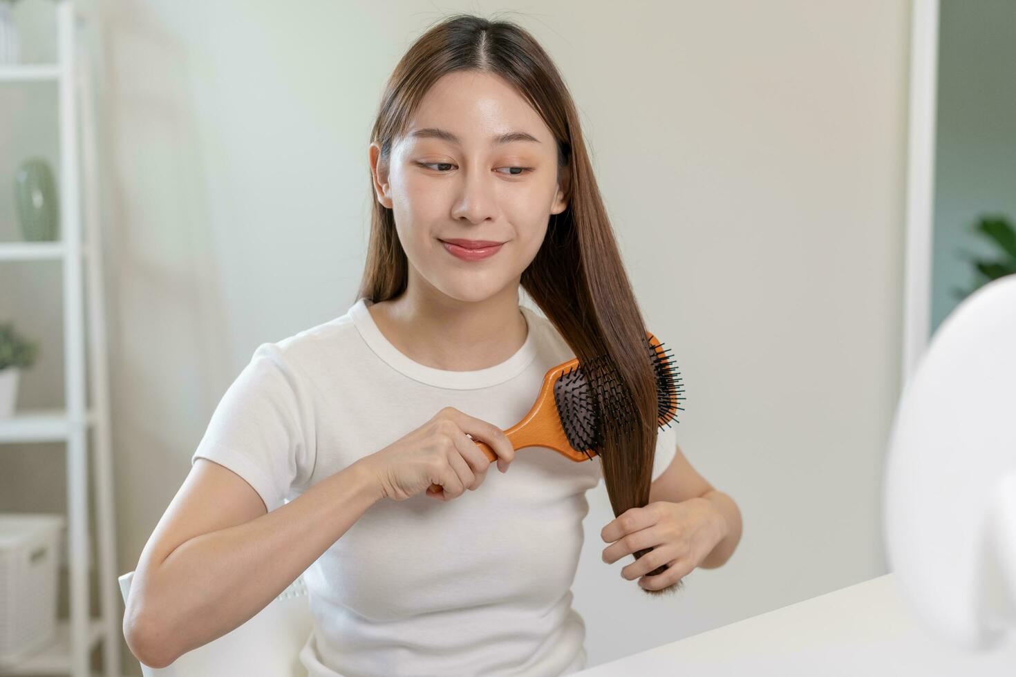 Salute capelli cura, bellezza trucco asiatico donna, ragazza Tenere spazzola per capelli e spazzolatura, pettinatura sua lungo dritto capelli guardare a riflessione nel specchio nel mattina routine dopo salone trattamento, acconciatura. foto