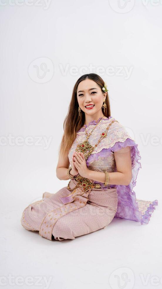 giovane asiatico donna indossare tipico tailandese vestito e in posa per pagare rispetto con sorridente isolato su bianca sfondo, identità cultura di Tailandia foto