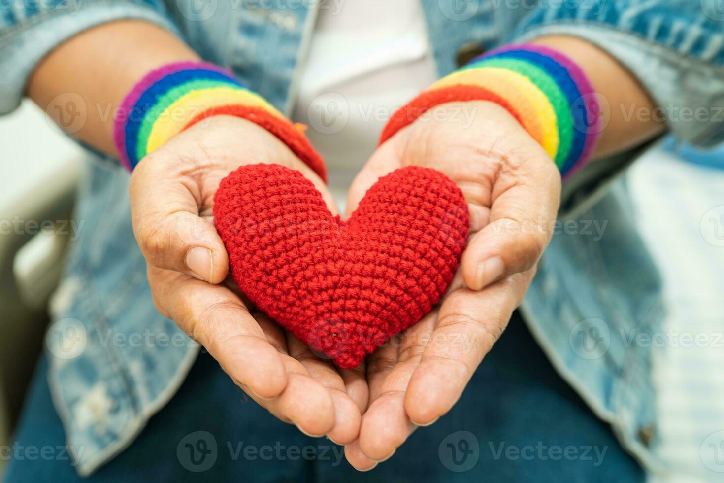 la signora asiatica che indossa braccialetti con bandiera arcobaleno e tiene il cuore rosso, simbolo del mese dell'orgoglio lgbt celebra l'annuale a giugno sociale di gay, lesbiche, bisessuali, transgender, diritti umani. foto