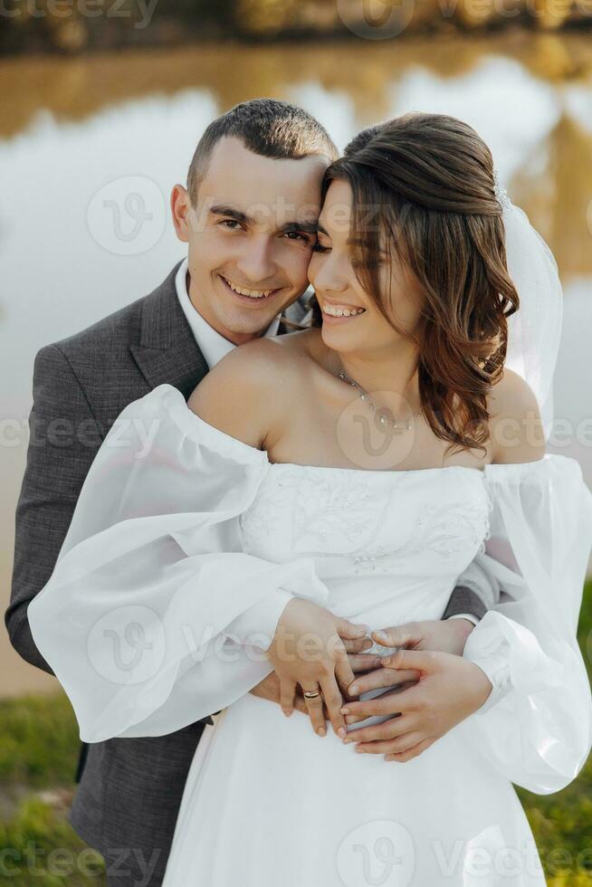 elegante bellissimo coppia. il sposo abbraccia il sposa. lei amorevolmente Appoggiato contro lui. meraviglioso leggero Aggiunge per il romantico atmosfera. il sposa e sposo Sorridi magnificamente. foto