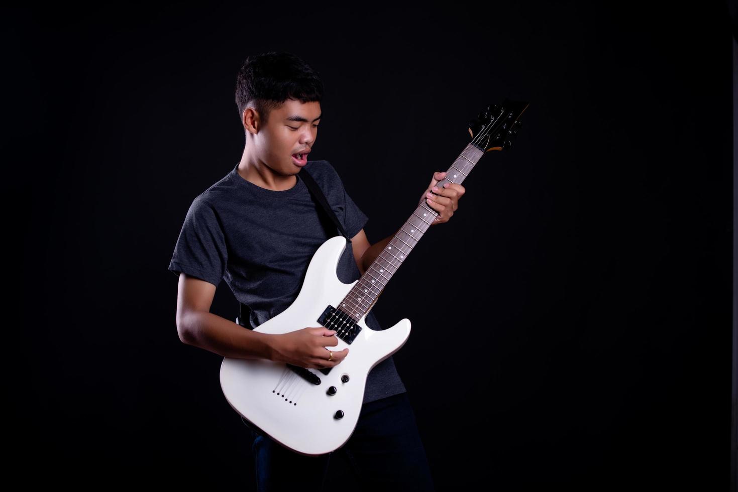 giovane uomo in giacca di pelle nera con chitarra elettrica su sfondo nero in studio foto