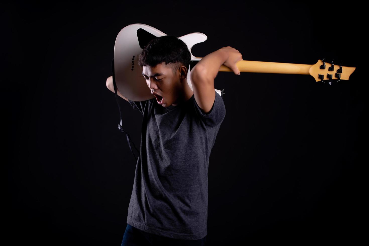 giovane uomo in giacca di pelle nera con chitarra elettrica su sfondo nero in studio foto