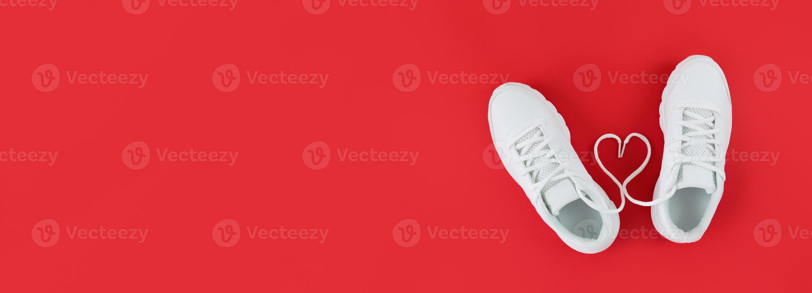 scarpe sportive bianche e forma di cuore da lacci su uno sfondo rosso semplice piatto disteso con spazio di copia foto