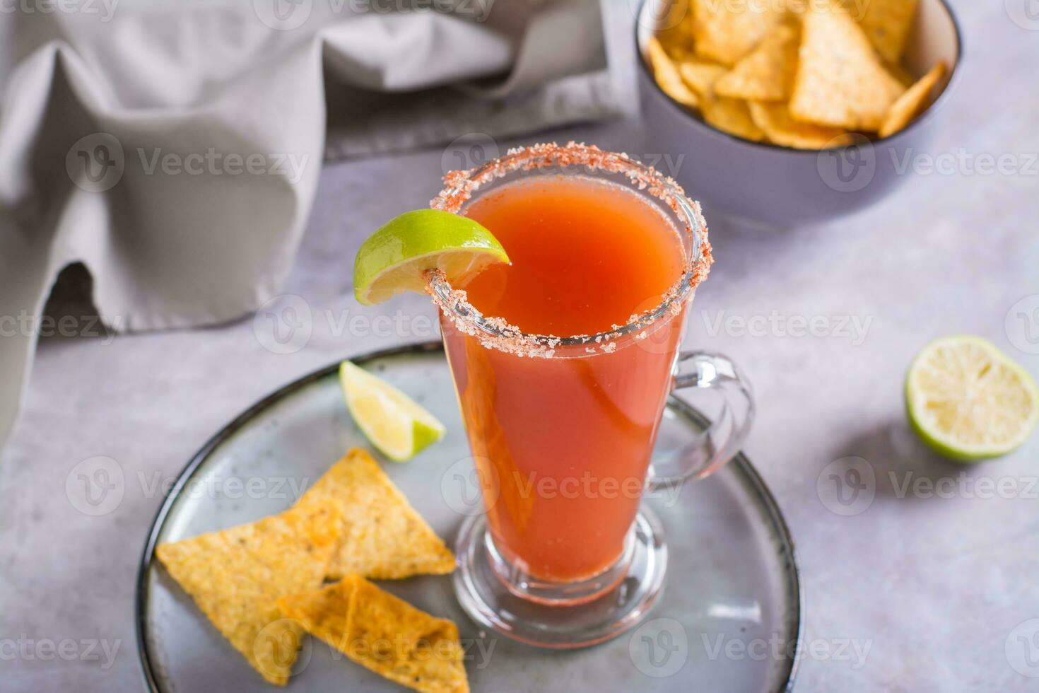 michelagua mocktail con pomodoro succo e lime succo nel un' bicchiere e nachos nel un' ciotola foto