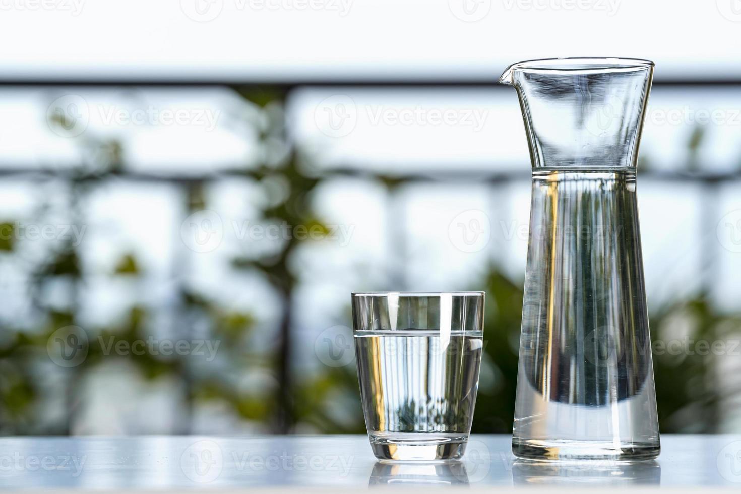 bere acqua in una brocca di vetro con il bicchiere sul tavolo in giardino a casa foto