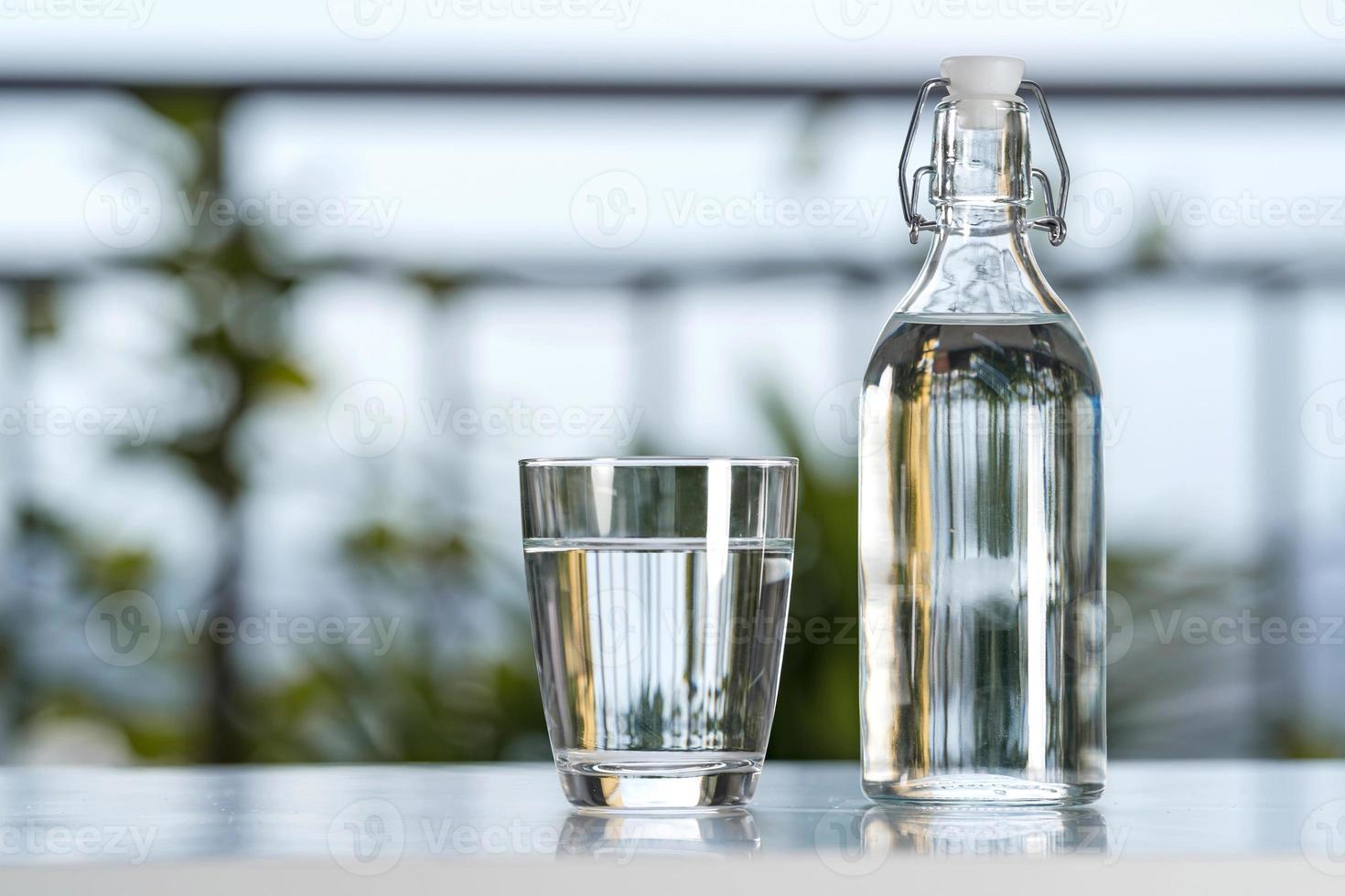 bevi una bottiglia d'acqua con un bicchiere sul tavolo a casa in giardino foto