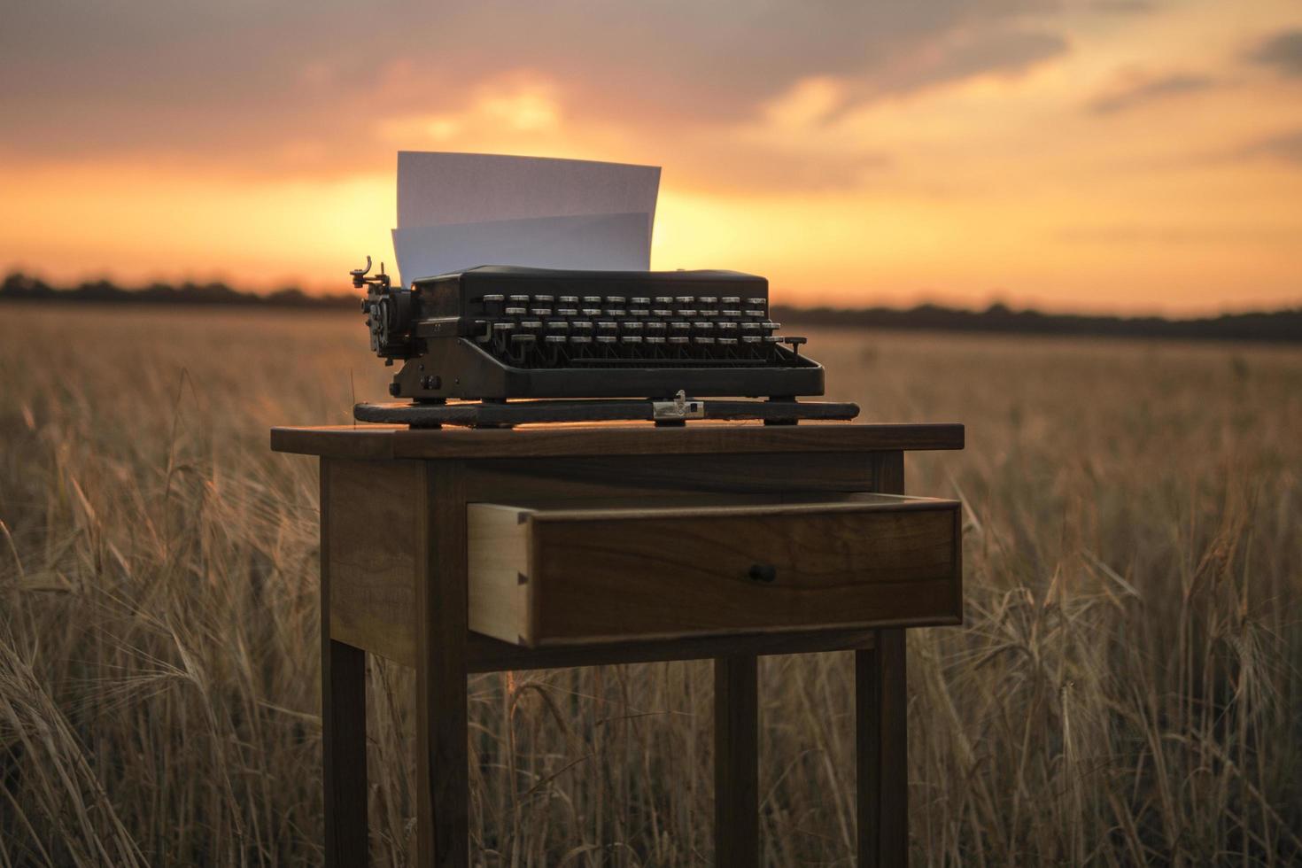 carta da parati macchina da scrivere su un comodino in noce in un campo di grano al tramonto foto