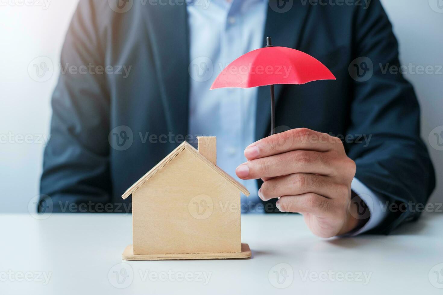 mano dell'uomo d'affari che tiene il modello domestico di legno della copertura dell'ombrello rosso. concetti immobiliari, assicurativi e di proprietà foto