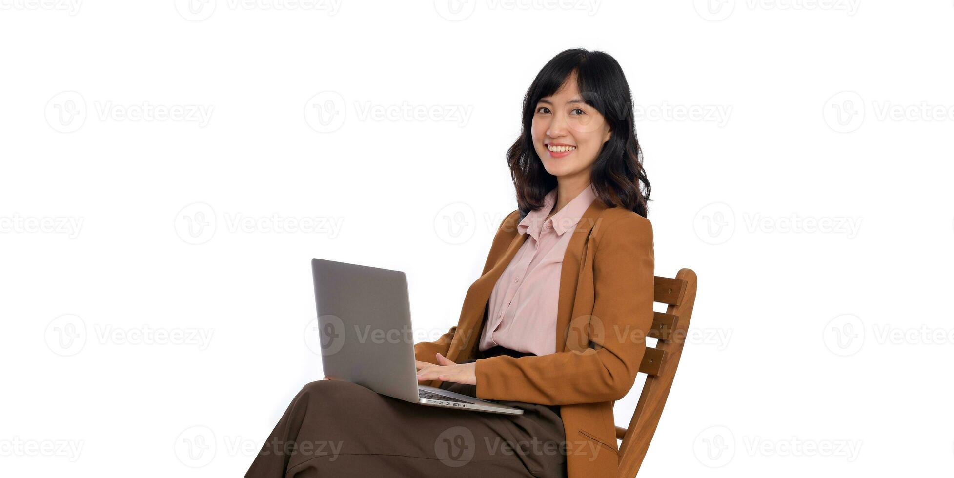 contento giovane attività commerciale asiatico donna sorridente. mentre sua utilizzando il computer portatile seduta su di legno sedia isolato su bianca sfondo foto